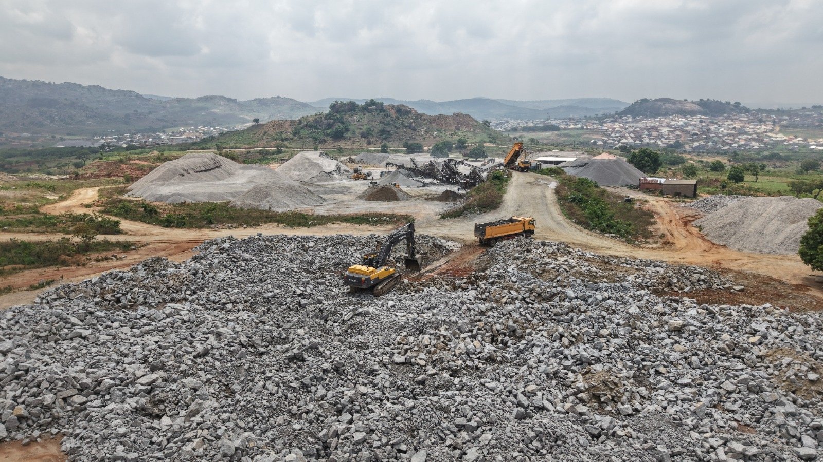 Excavator working across granite rock and aggregate stockpiles at Jikoko quarry